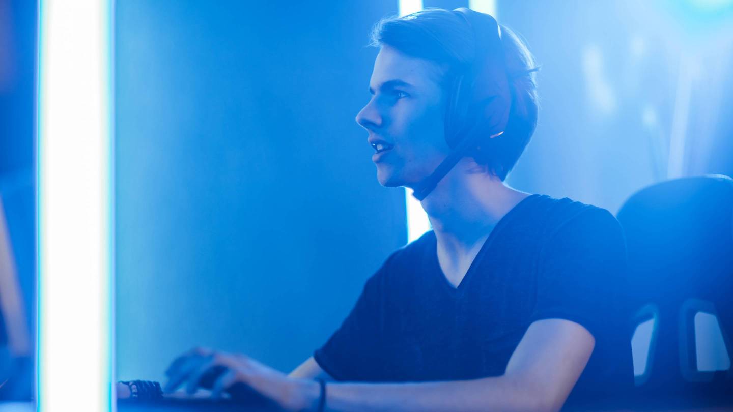 Shot of the Pro Gamer Playing in Video Games on His Personal Computer. Talking with His Team through Microphone on Headphones. Retro Neon Room.