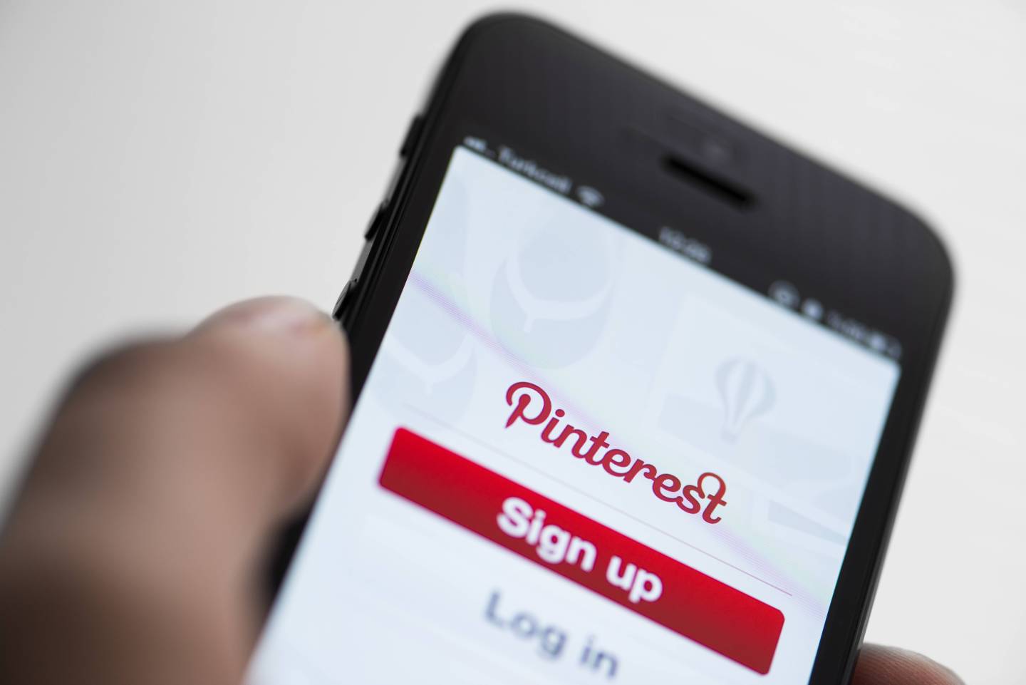 A woman's hand holds an iPhone with the Pinterest app open.