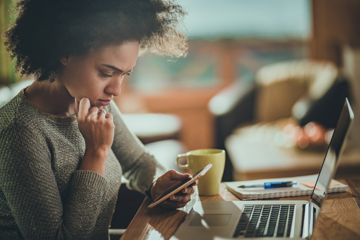Young black woman reading problematic text message on her mobile phone while working at home.
