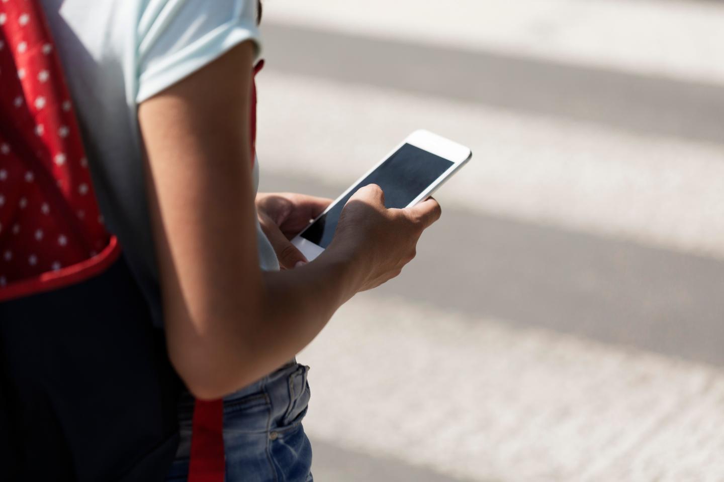 Close-up on a kid with a smartphone while walking through pedestrian crossing