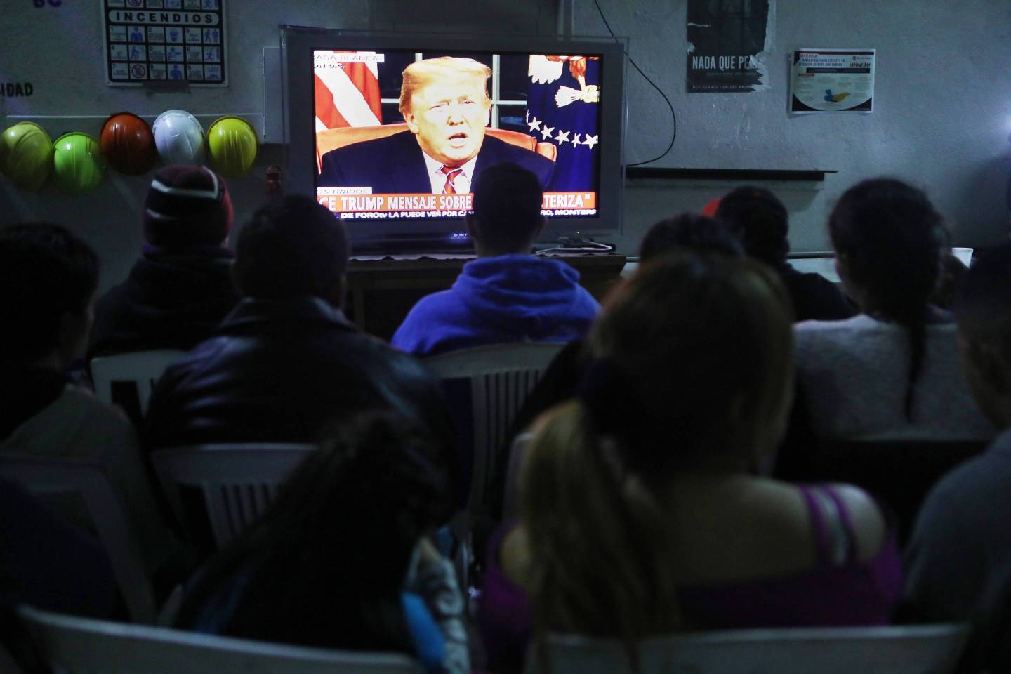 Migrants view a live televised speech by President Donald Trump on border security at a shelter on Jan. 8, 2019 in Tijuana, Mexico.