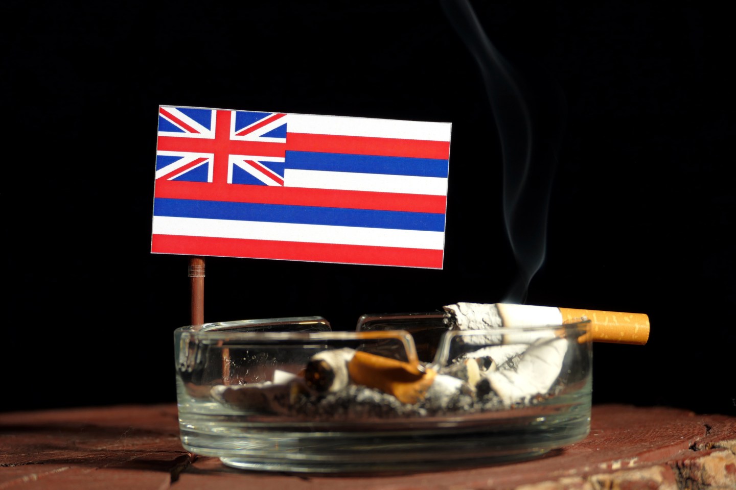 Hawaii flag with burning cigarette in ashtray isolated on black background
