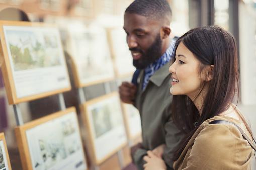 Smiling young couple looking at real estate listings at storefront