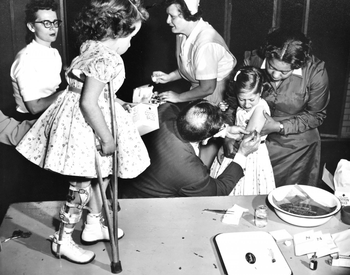 Joanne Wilson looks on as her friend Roslyn Feigenbaum gets a polio vaccine.