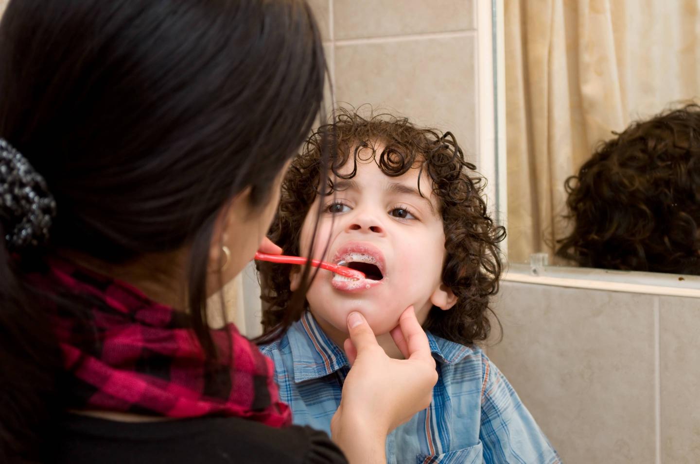 Mother brushing teeth her little boy with a toothbrush in