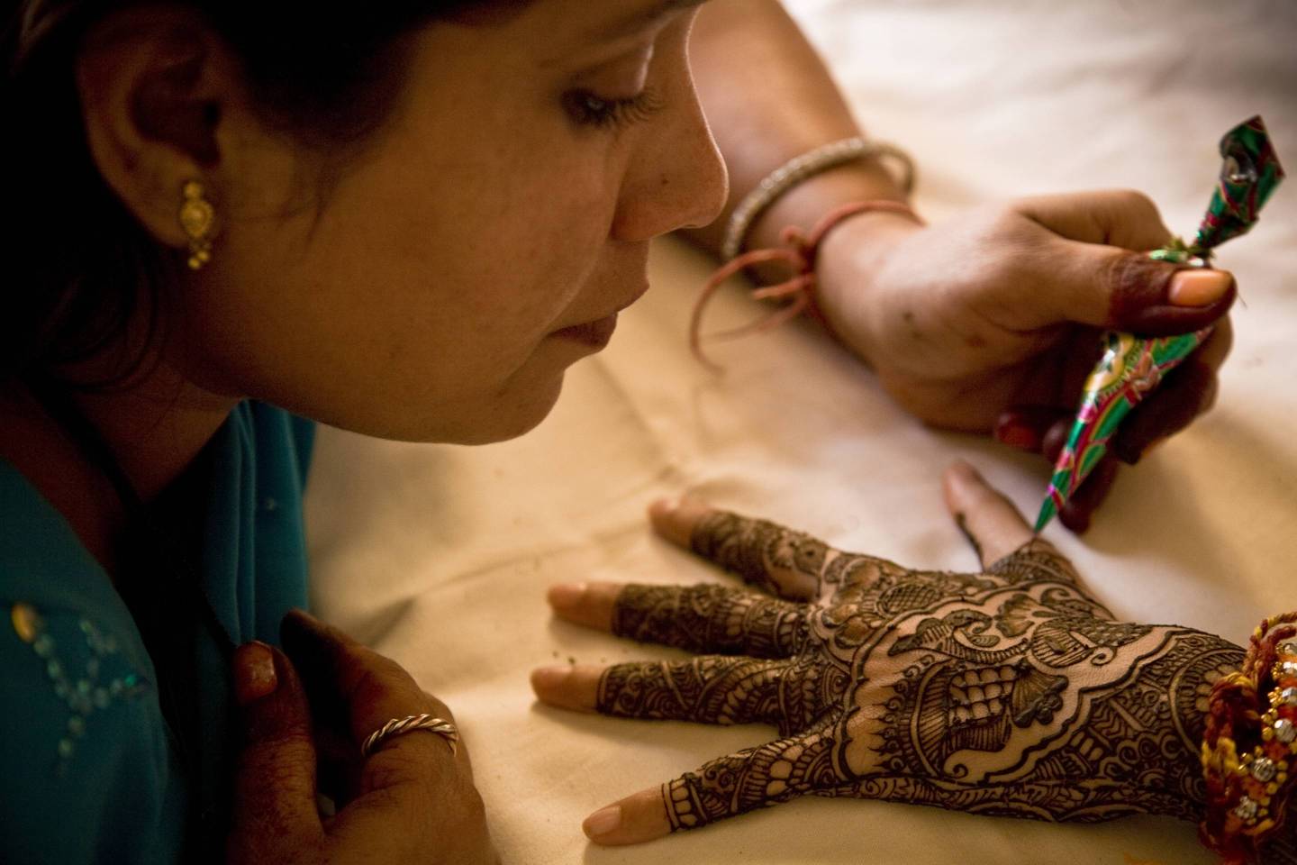 A young bride lies on her bed as she has henna decorated onto her hand by a local artist in preparation for her wedding ceremony in Jaipur, India.