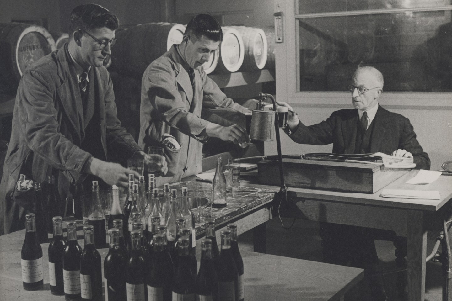 Album page from album entitled `St. James`s Gate Brewery, 3`. Black and white. Interior view of the brewers' Sampling Room with two men (Mick Kiersey on left and Joe Breslin in centre) preparing samples and one man seated testing a sample. Taken by A.R. Turner Esquire of Fox Photos Limited.