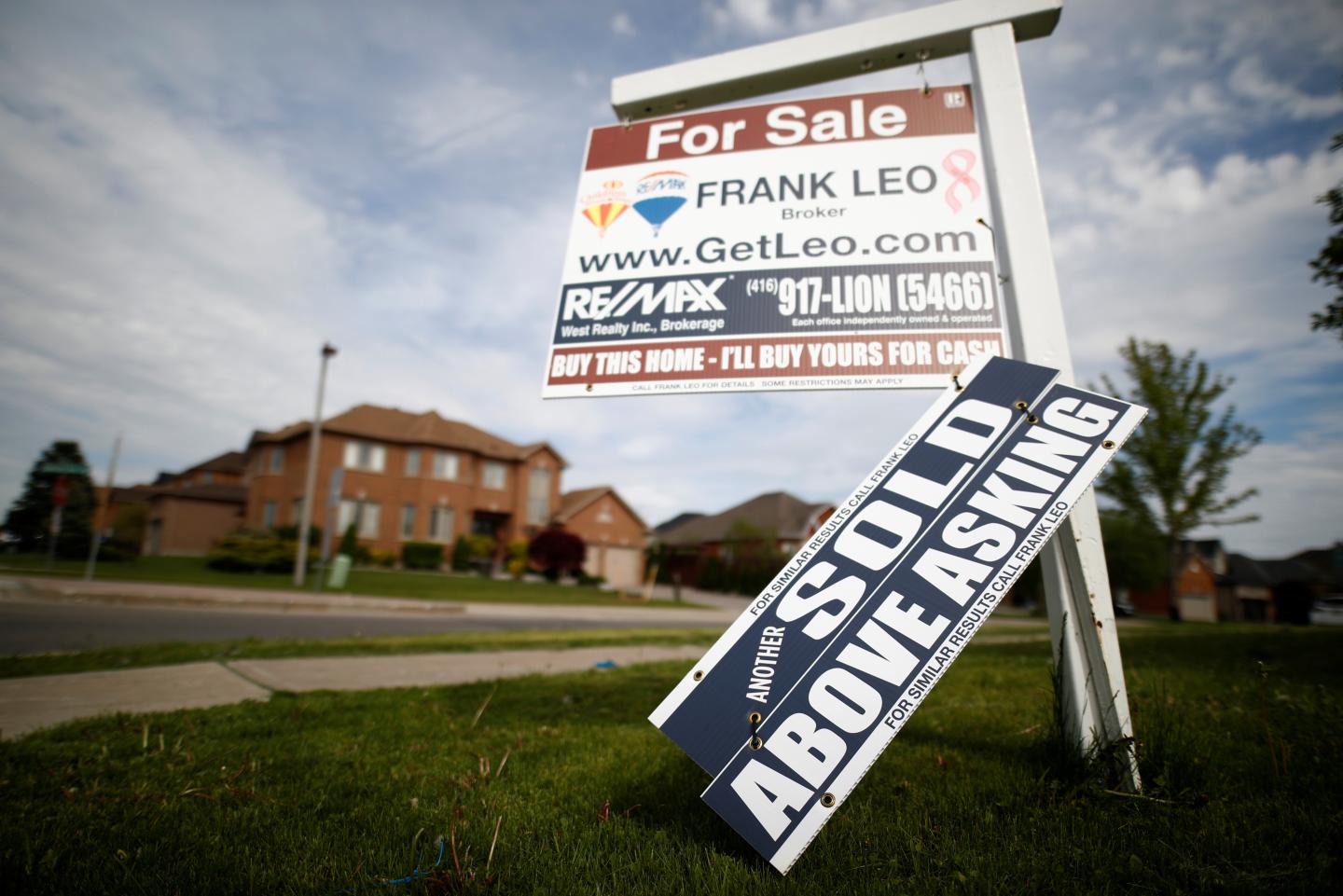 A real estate sign that reads "For Sale" and "Sold Above Asking" stands in front of housing in Toronto