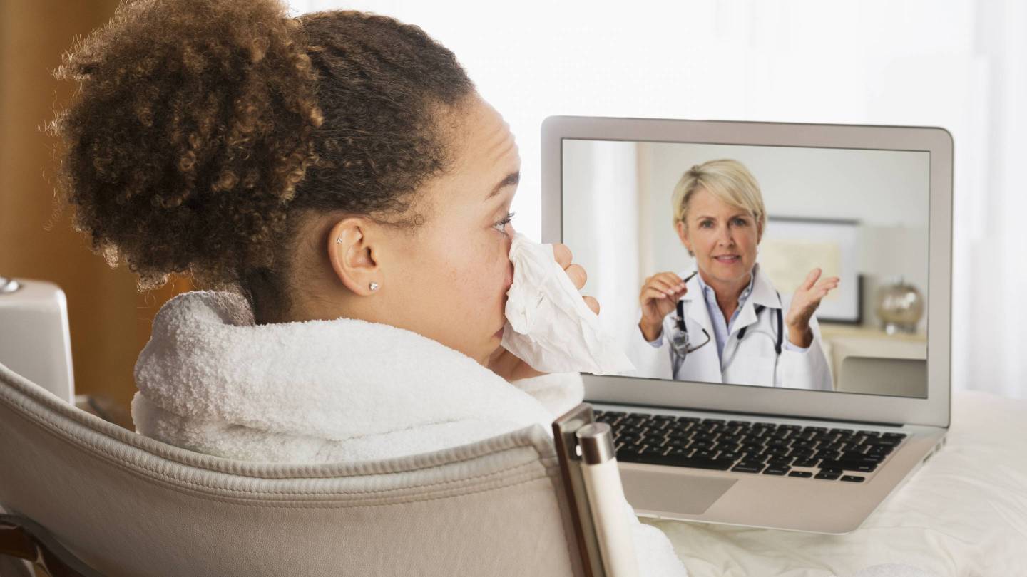 A sick woman video chats with her doctor on her laptop.