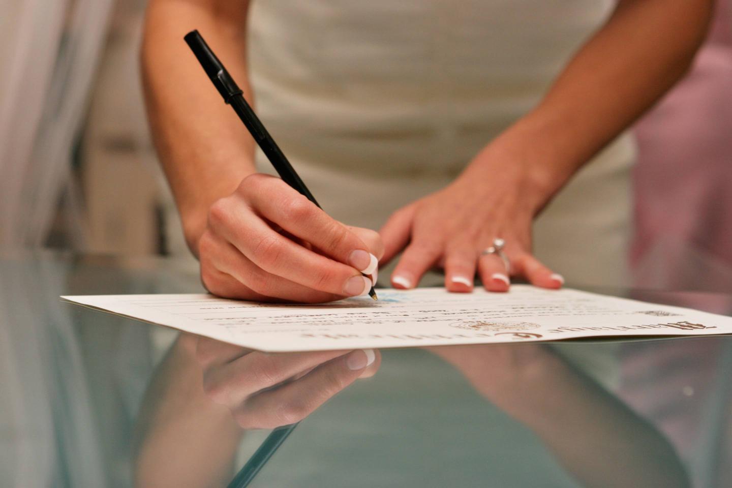 Bride Signing Wedding Certificate Reflection on Glass Table