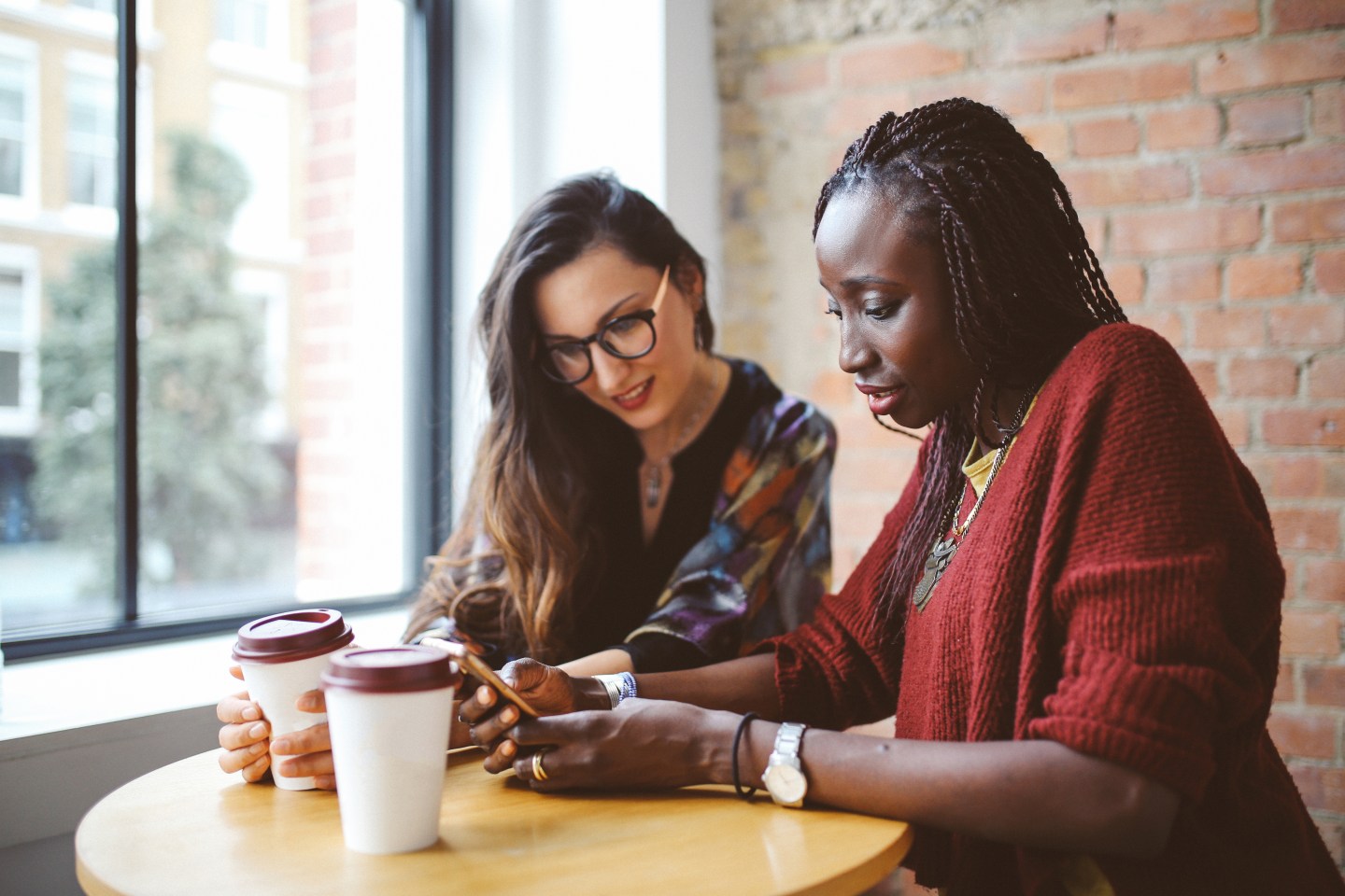 Portrait of a two young women of different ethnicities, working together in a cafe, looking at the laptop.