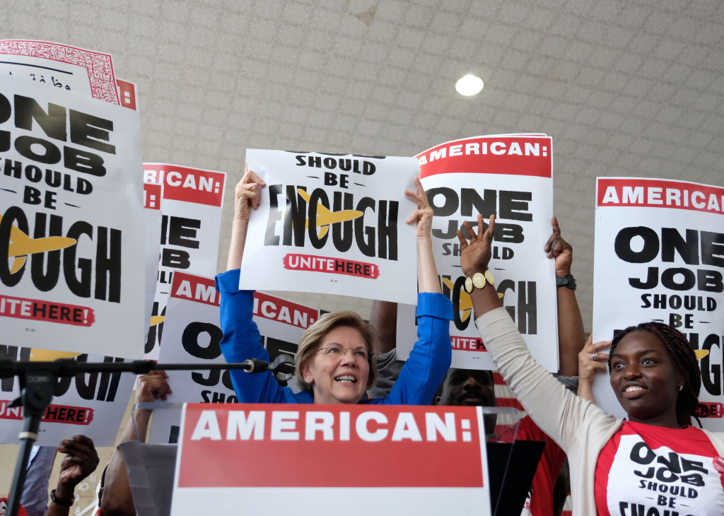 Senator Elizabeth Warren holds a sign while speaking during a rally with striking airline food workers at Reagan National Airport in Arlington, Virginia, U.S., on Tuesday, July 23, 2019.