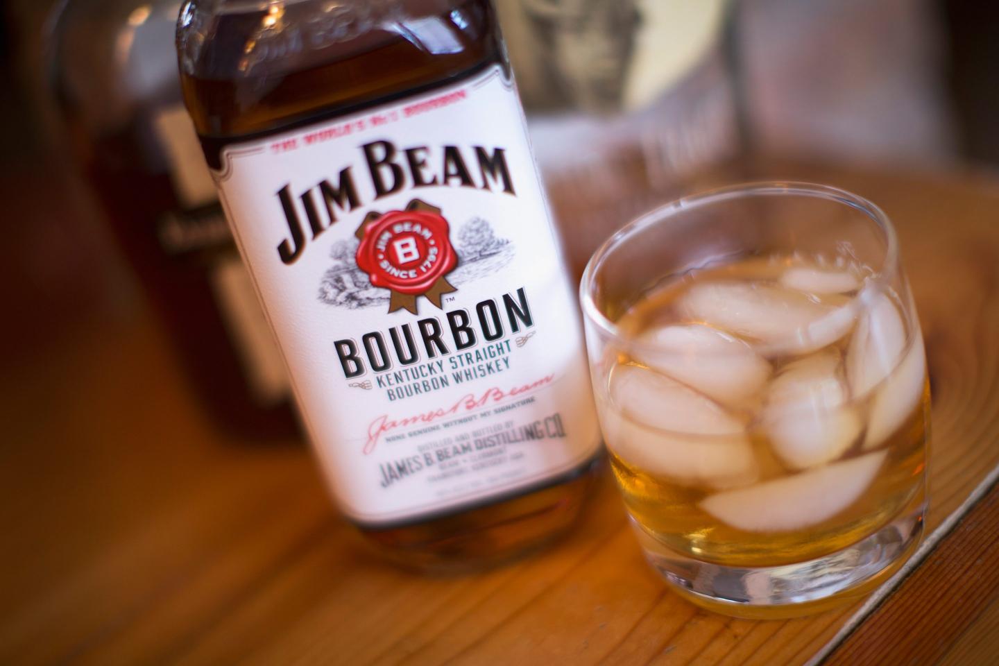 A bottle of Jim Beam bourbon sitting next to a glass of bourbon on the rocks