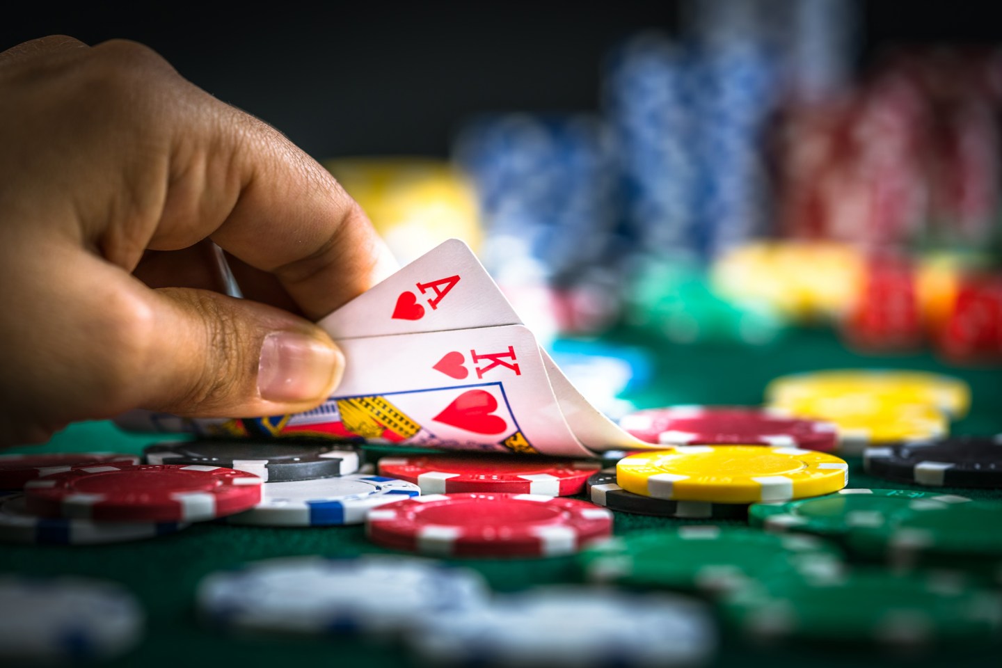 Gambler's hand holding ace and king of hearts with poker chips on the table.