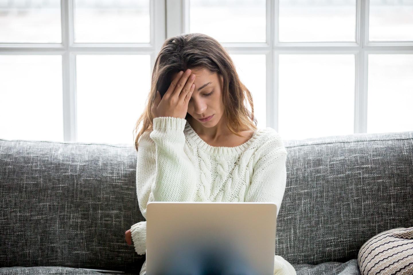 Frustrated woman using laptop on sofa