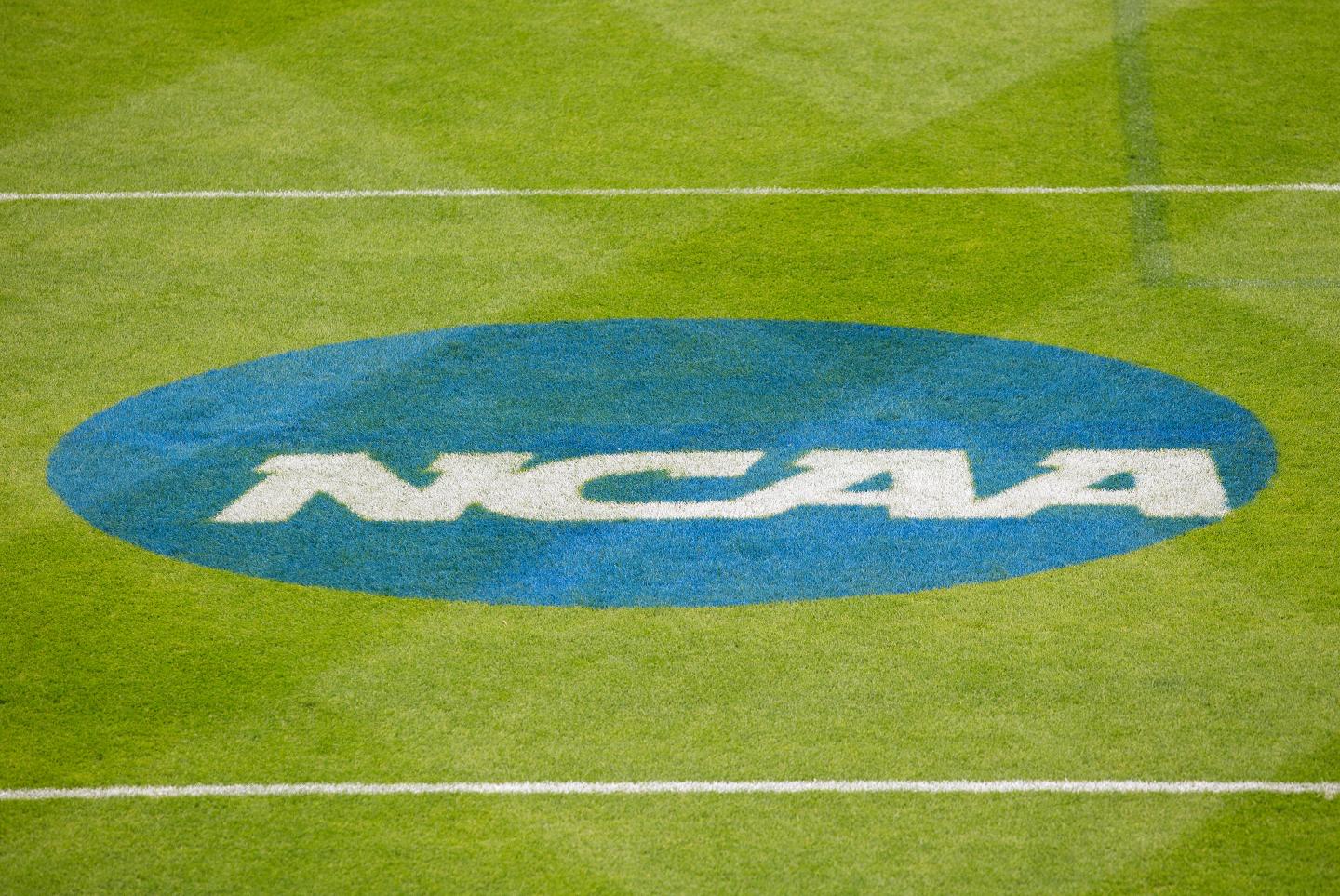 NCAA logo of white text in a blue circle printed on a sports field