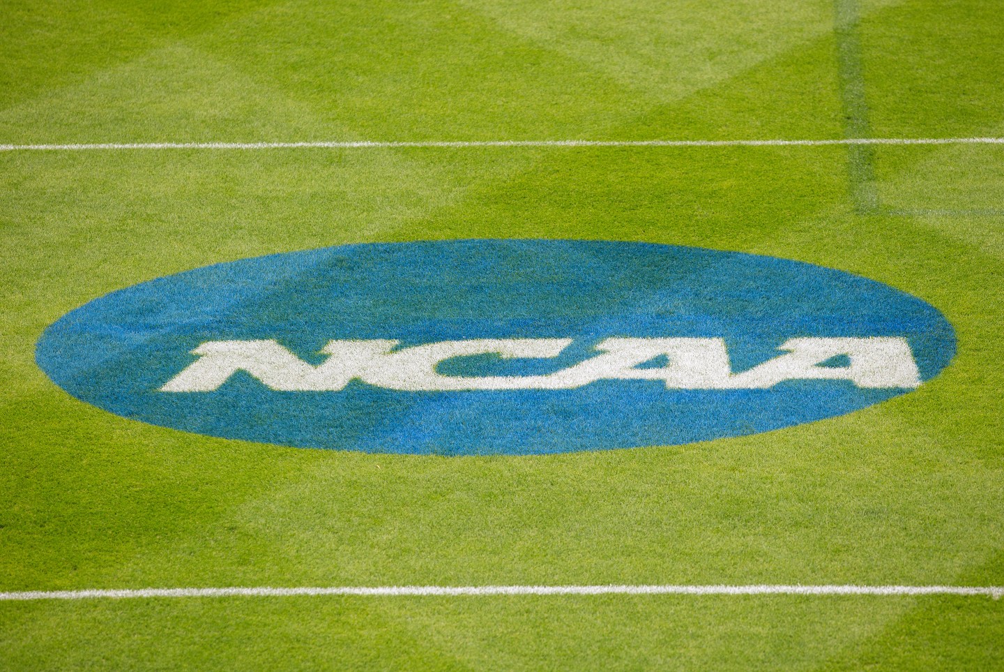 NCAA logo of white text in a blue circle printed on a sports field
