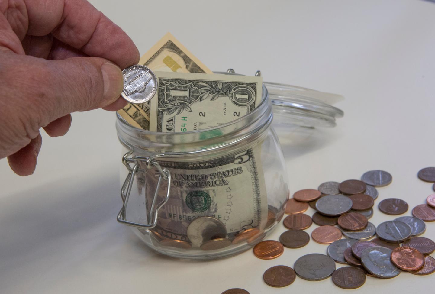 A hand drops a nickel into a savings jar