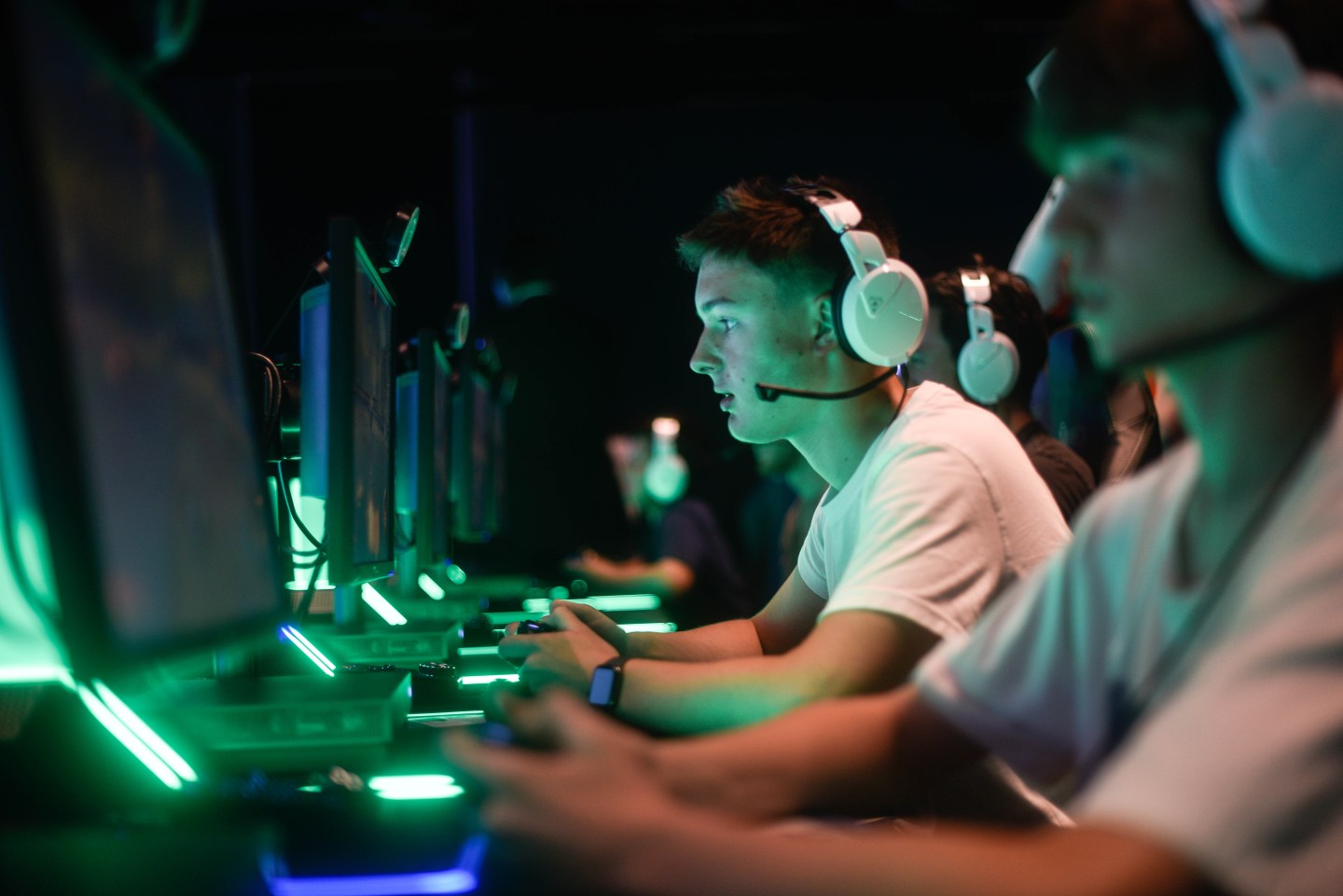 Three people wear video-game headsets in front of computers.