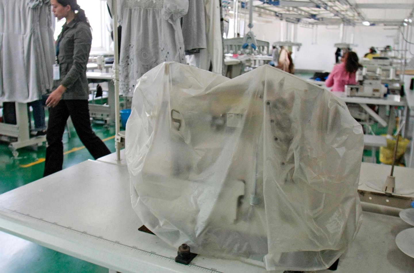 A woman walks past a sewing machine at the Ever-Glory Intern