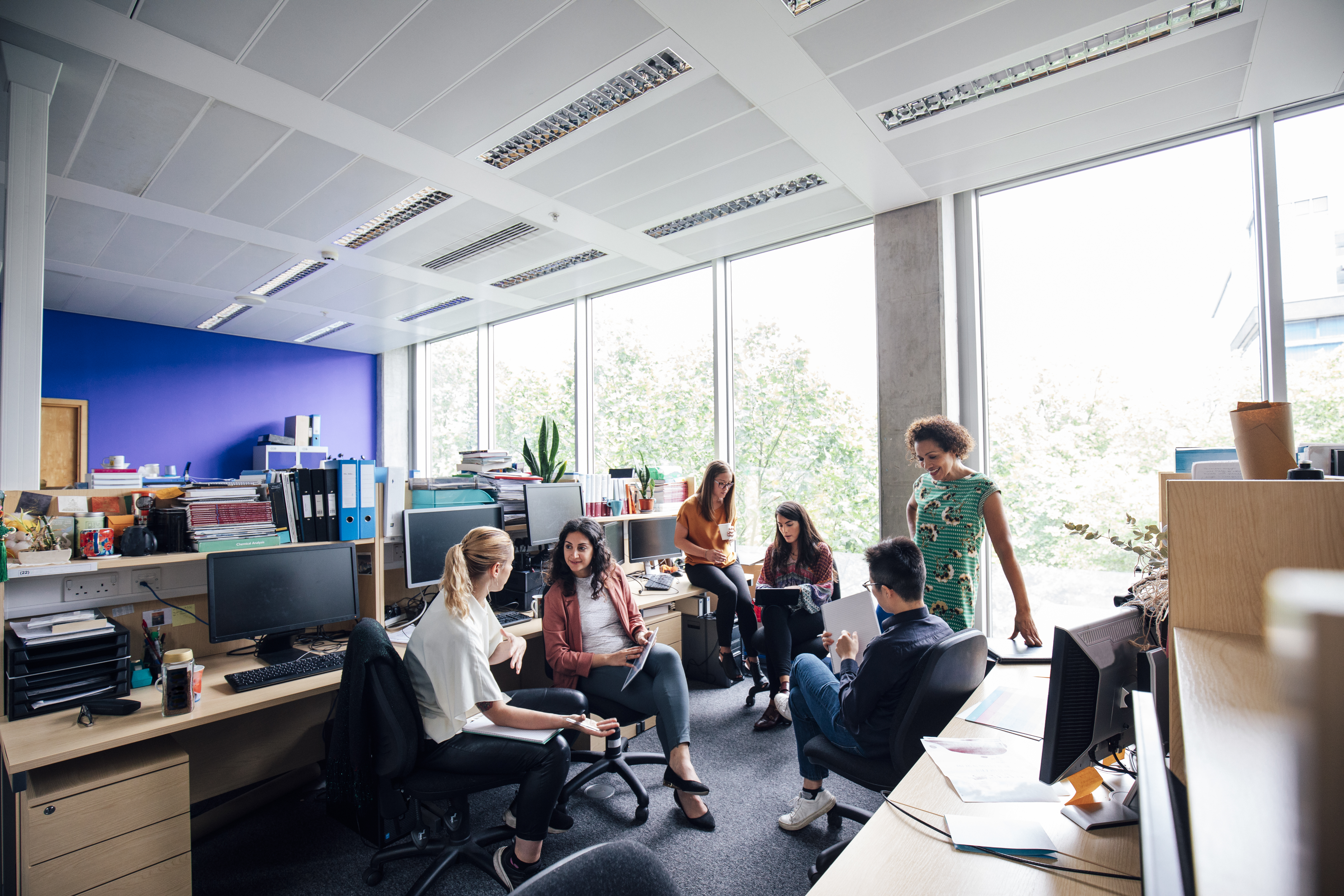 Superviser and staff, have an informal meeting around their desks.