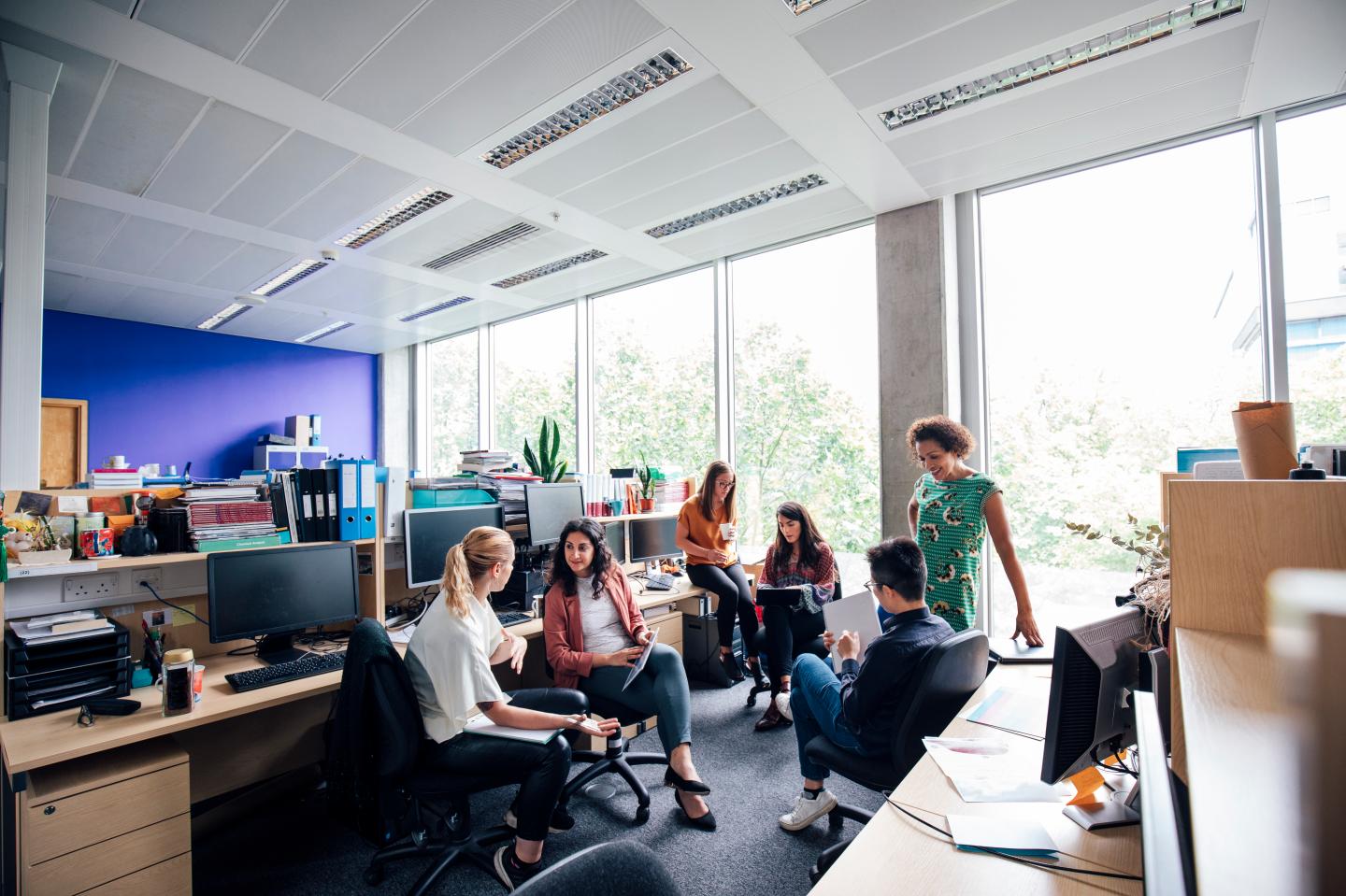 Superviser and staff, have an informal meeting around their desks.