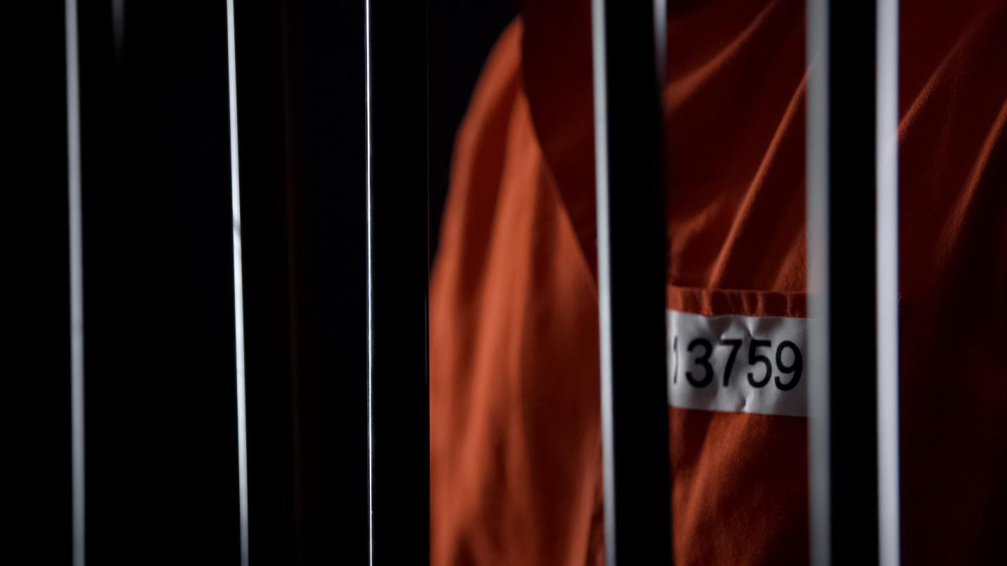 Prisoner in orange uniform standing behind bars