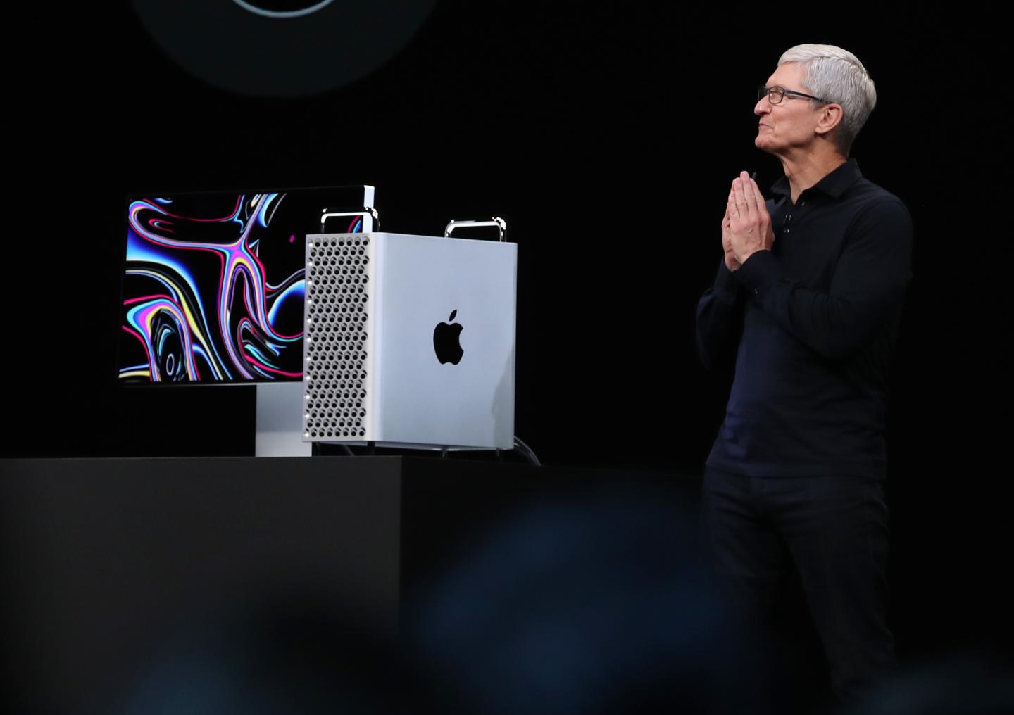 Tim Cook stands with hands pressed together next to the new Mac Pro, against a black background.