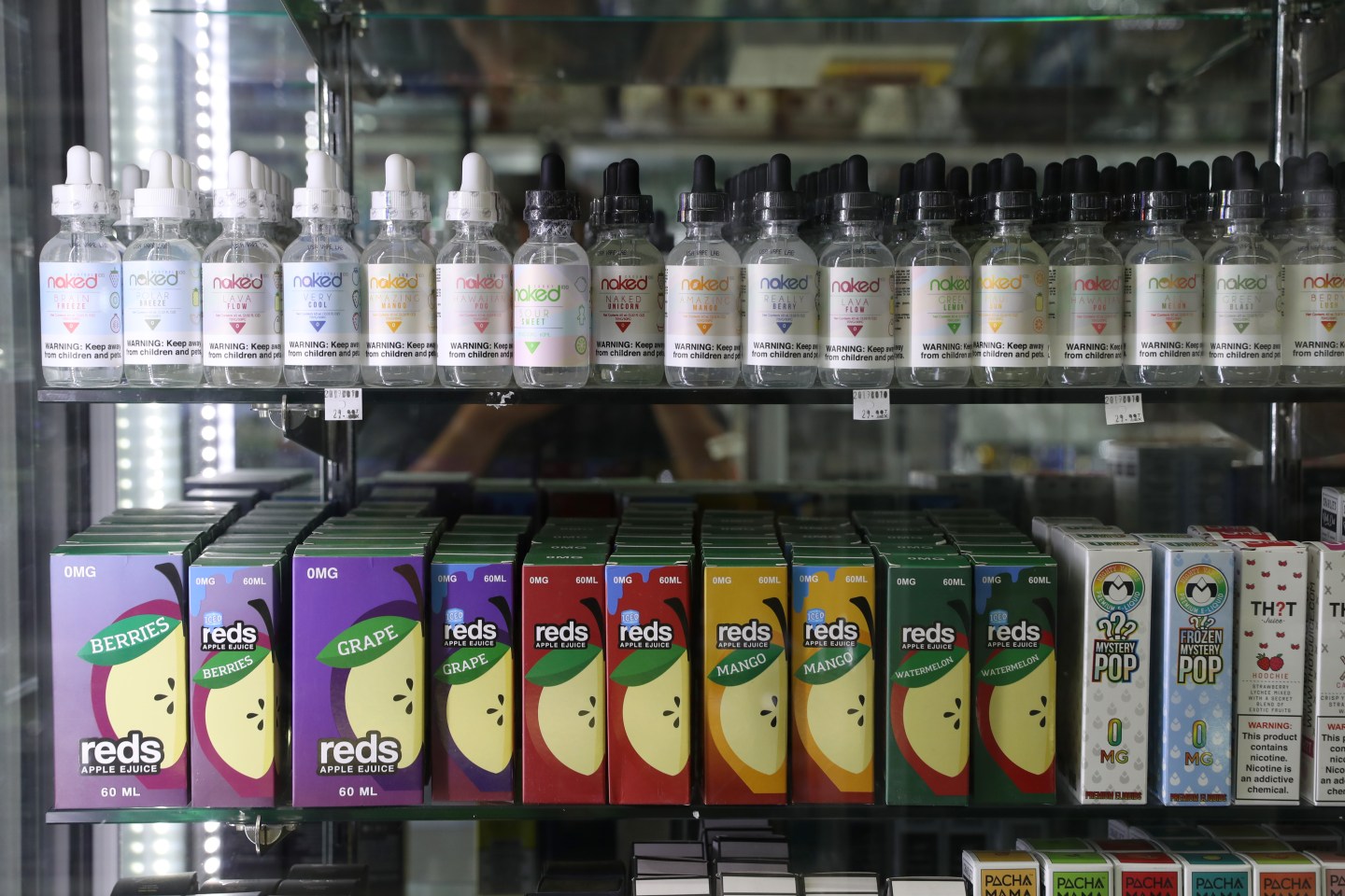 Boxes and dropper bottles of flavored vaping juices on two shelves.