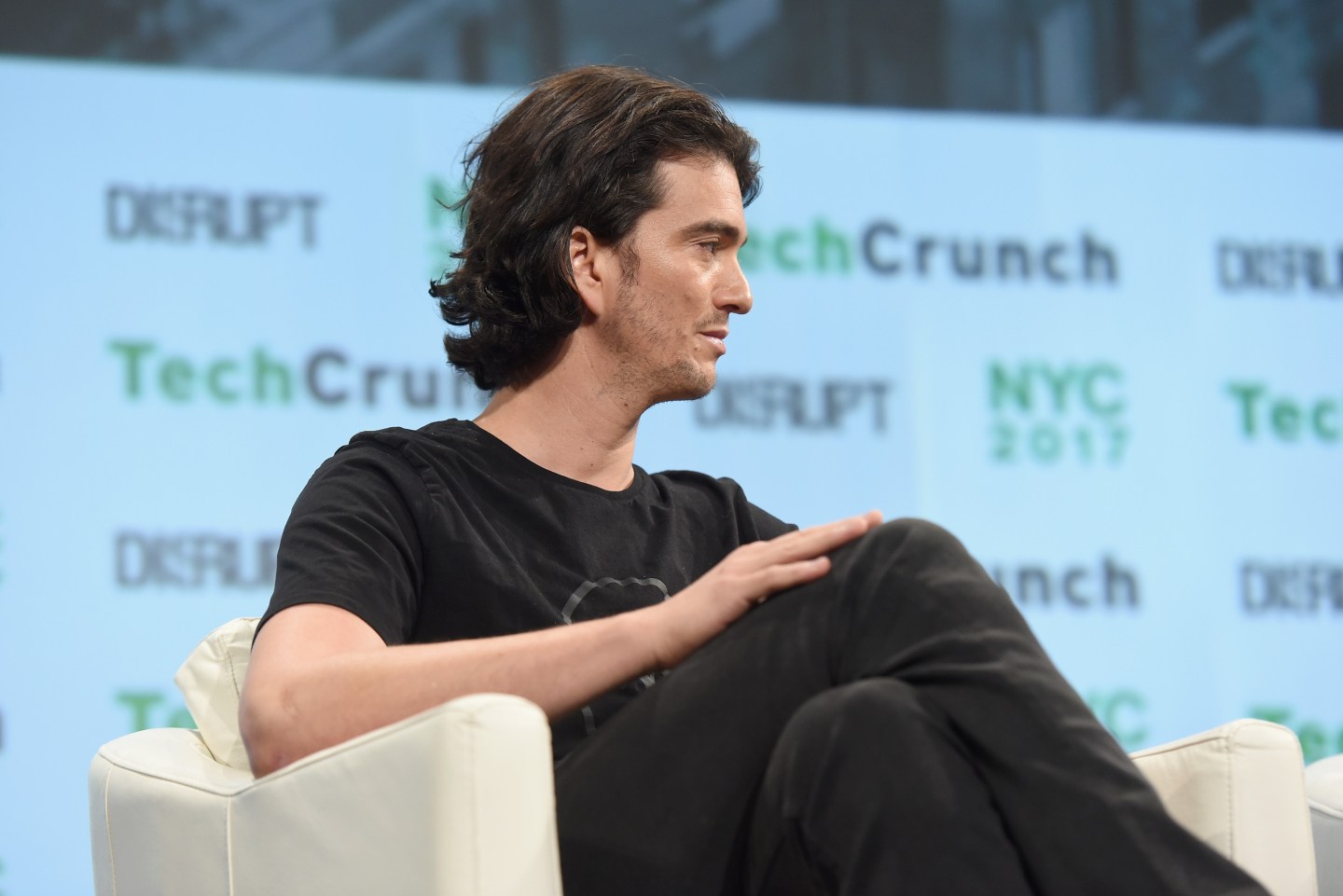 WeWork founder Adam Neumann sits in a chair turned away from the camera, showing his profile.