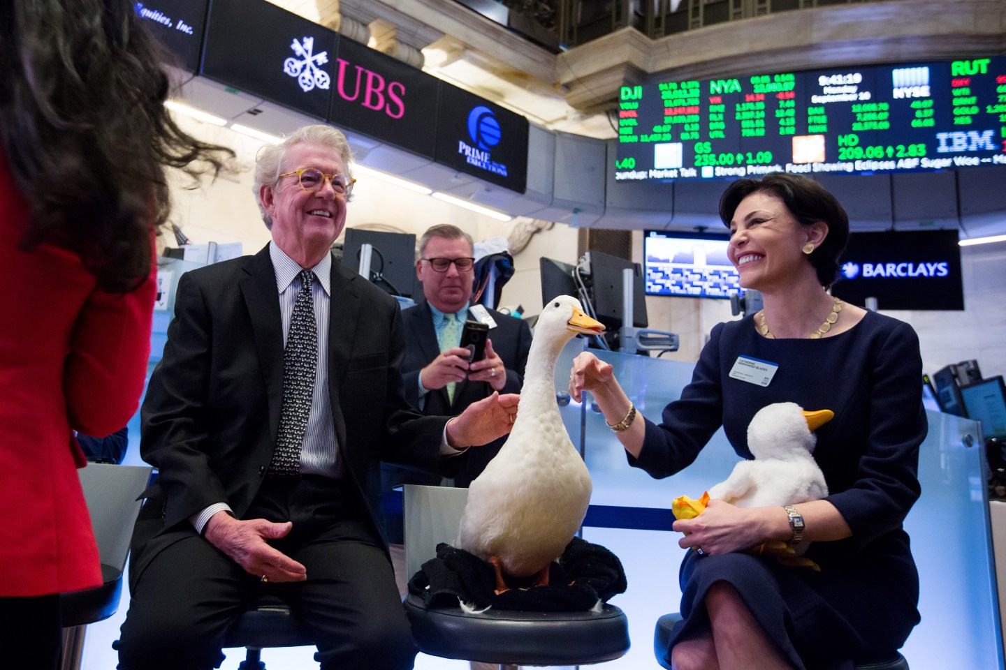 Dan Amos, chairman and chief executive officer of Aflac Inc., left, and Catherine Hernandez-Blades, chief brand and communications officer of Aflac Inc., right, pet the Aflac duck on the floor of the New York Stock Exchange (NYSE) in New York, U.S., on Monday, Sept. 10, 2018.