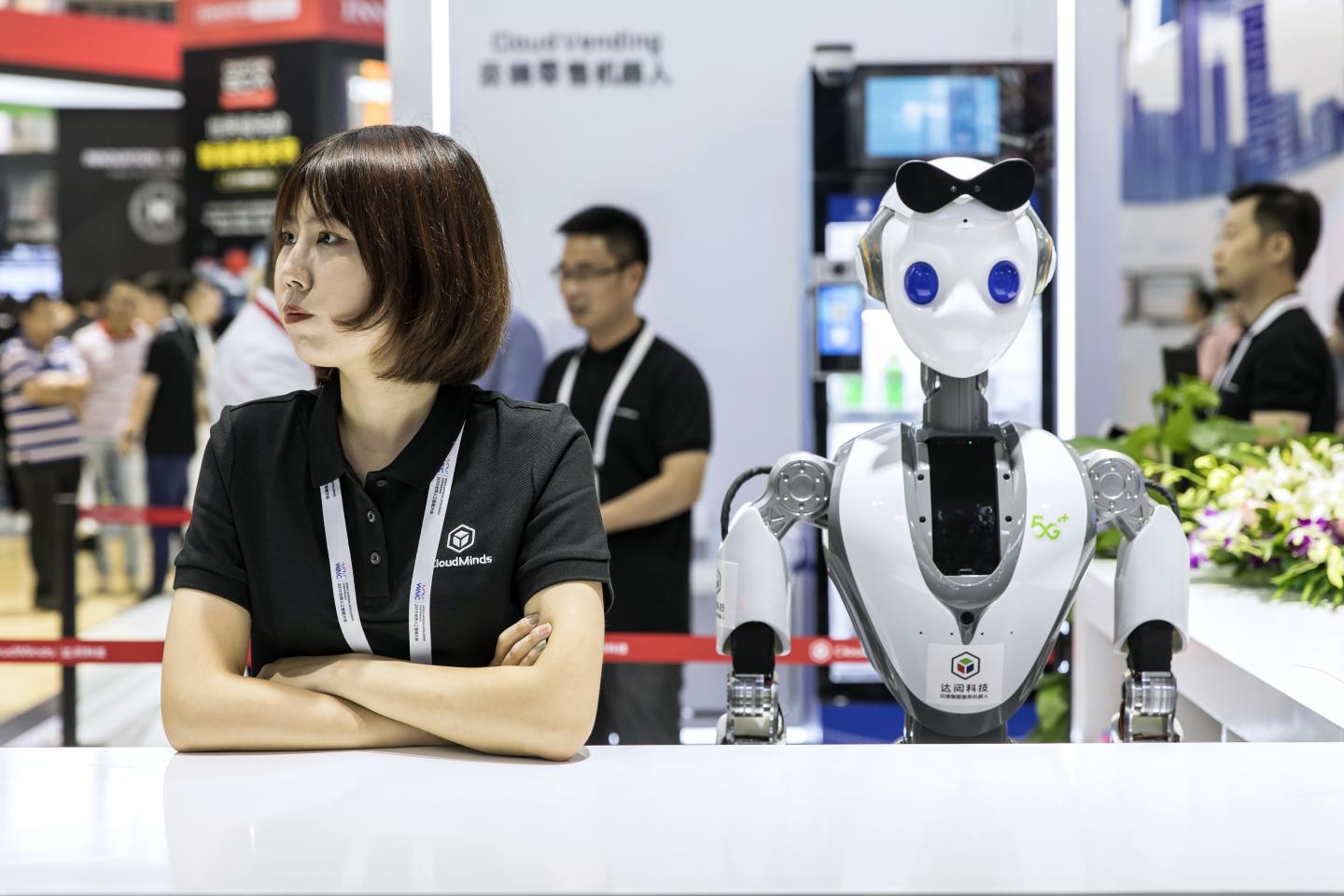 An attendant stands next to a CloudMinds Technology Inc. XR-1 commercial humanoid service robot at the World Artificial Intelligence Conference (WAIC) in Shanghai, China, on Thursday, Aug. 29, 2019.