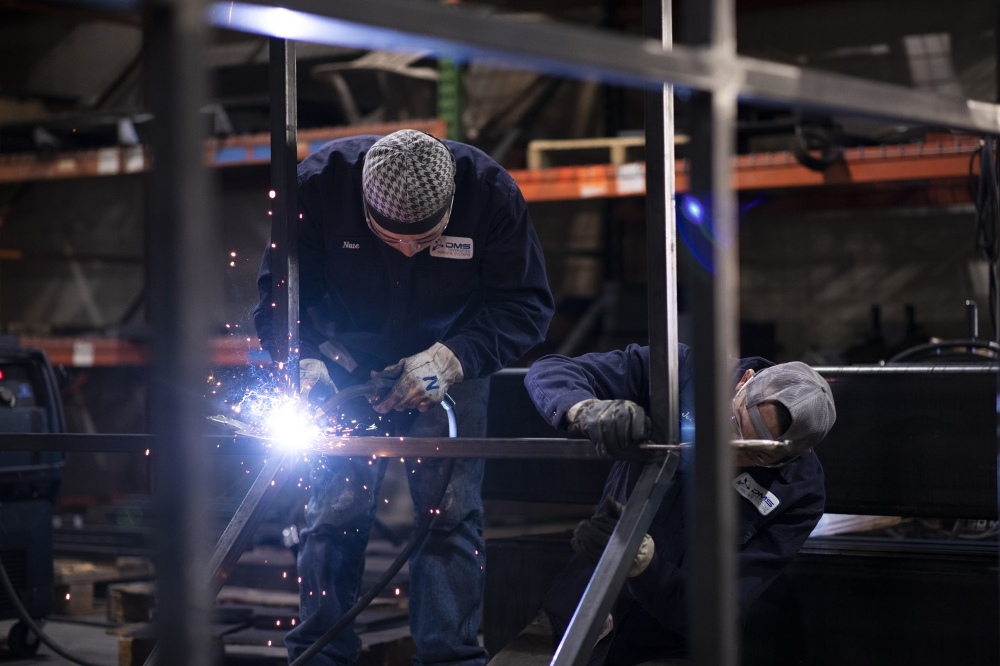 Two employees prepare a steel frame with a large spark emitting from a tool