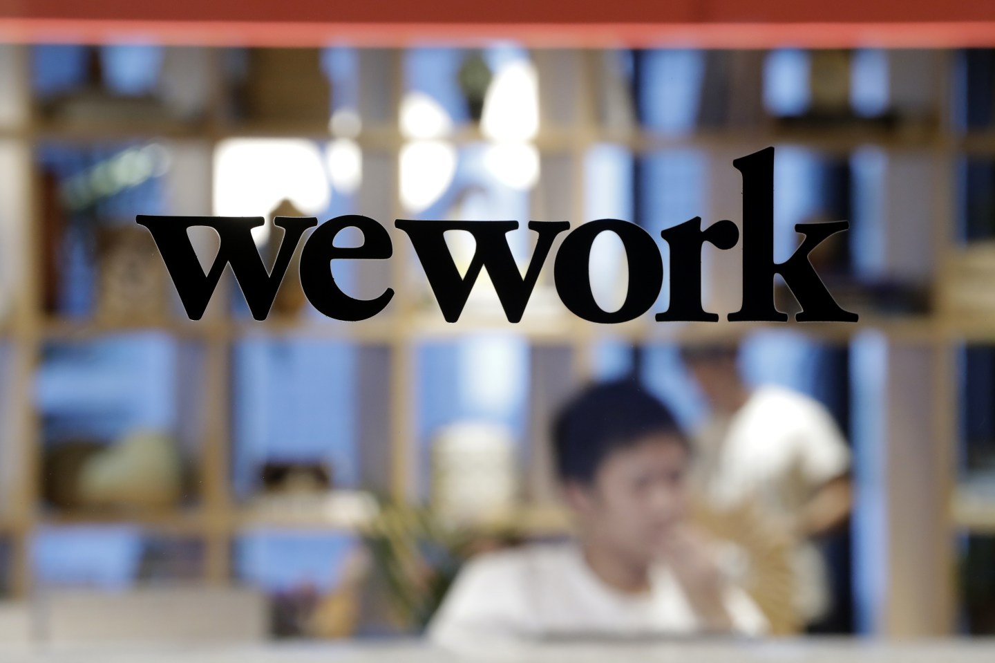 The WeWork logo sits on display on a glass door of the entrance to the WeWork Ocean Gate Minatomirai co-working office space, operated by The We Company, in Yokohama, Japan, on Friday, Oct. 11, 2019. WeWork formally withdrew the prospectus for an IPO this month, capping a botched fundraising effort that cost its top executive his job. The defeat places urgency on WeWork to find new sources of capital to keep its business running Photographer: Kiyoshi Ota/Bloomberg via Getty Images