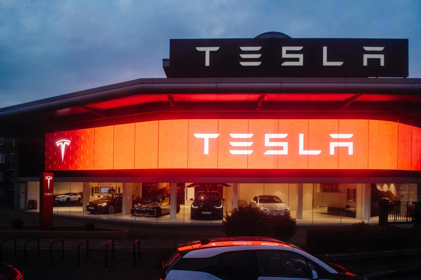 Street view of Tesla motors showroom with cars inside and illuminated logo brandin at dusk London UK