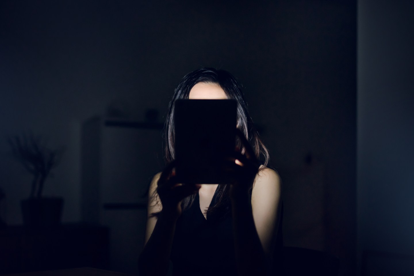 Woman with digital tablet covering up her face in the dark