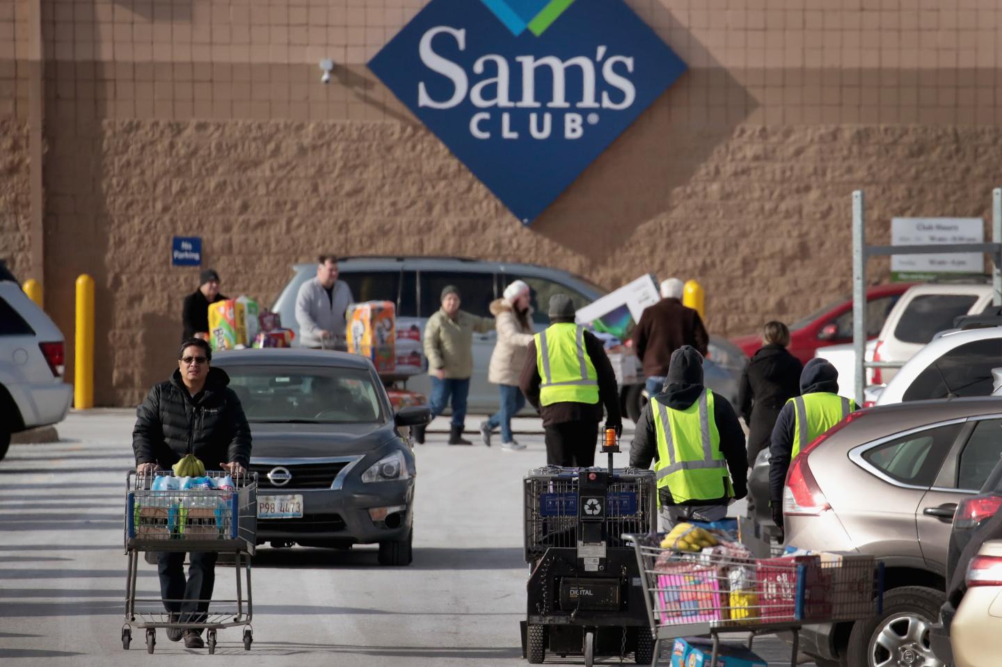People bundled up for cold weather enter and leave a Sam's Club through a parking lot.