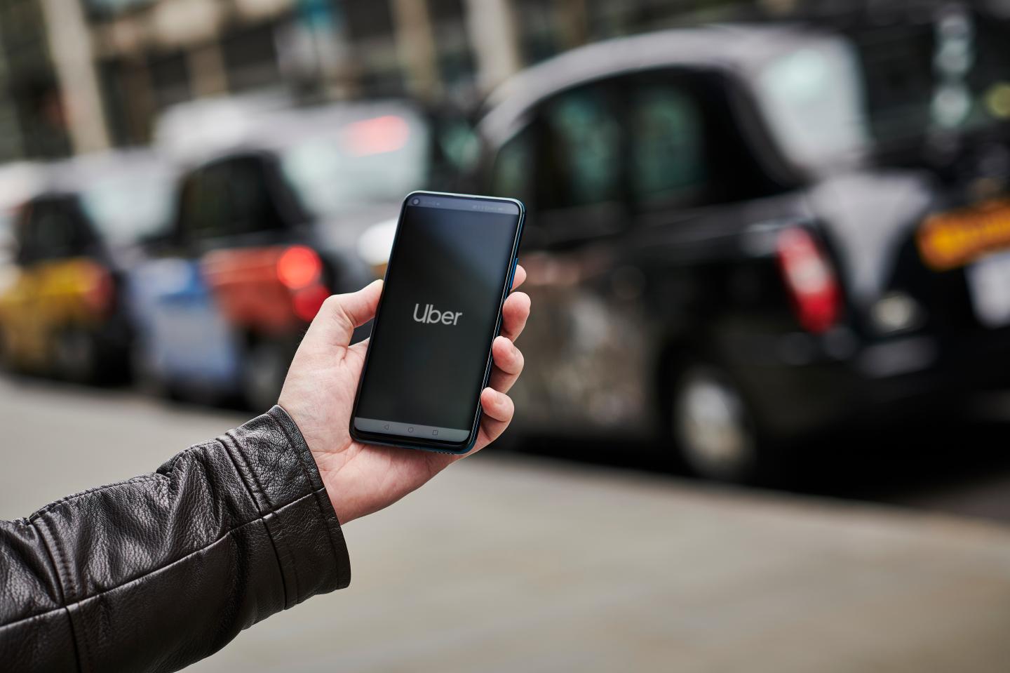 Detail of a man holding up an Honor 20 Pro smartphone with the Uber transport app visible on screen, while taxis queue in the background, on June 4, 2019.