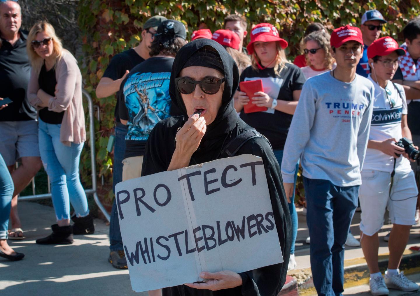 A Muslim woman holds a 'Protect Whistleblowers" sign as she walks past supporters of President Trump during a protest outside a book promotion by Donald Trump Jnr, at the UCLA campus in Westwood, California on November 10, 2019. (Photo by Mark RALSTON / AFP) (Photo by MARK RALSTON/AFP via Getty Images)