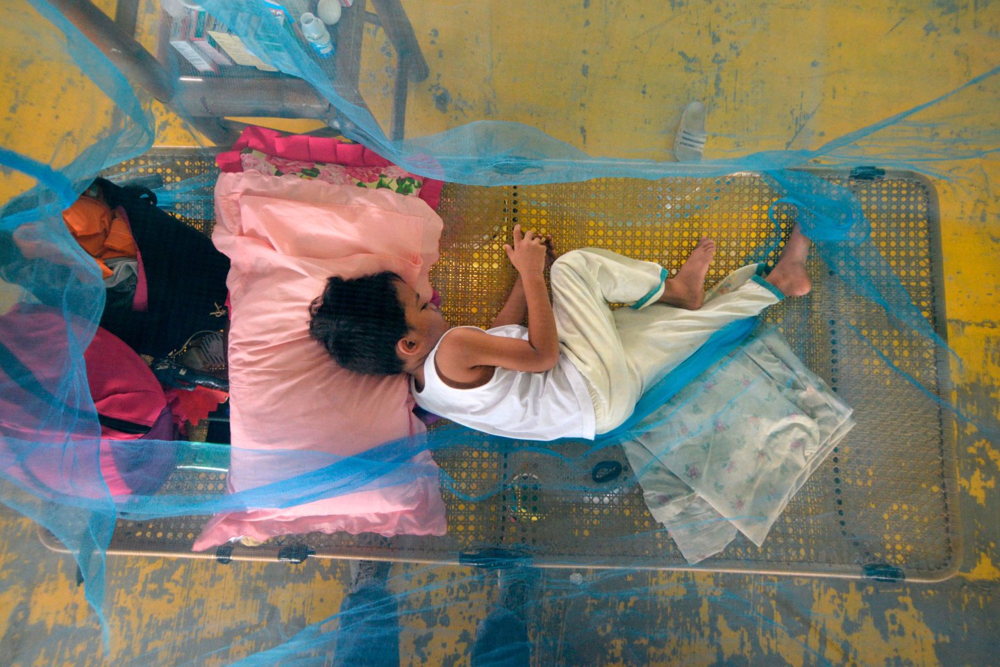 A boy suffering from dengue fever rests under a mosquito net in a gymnasium
