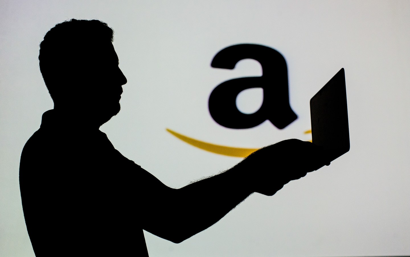 ANKARA, TURKEY - SEPTEMBER 1: Silhouette of a man holding a laptop is seen in front of the logo of 'Amazon' online shopping website in Ankara, Turkey on September 1, 2018. (Photo by Ali Balikci/Anadolu Agency/Getty Images)