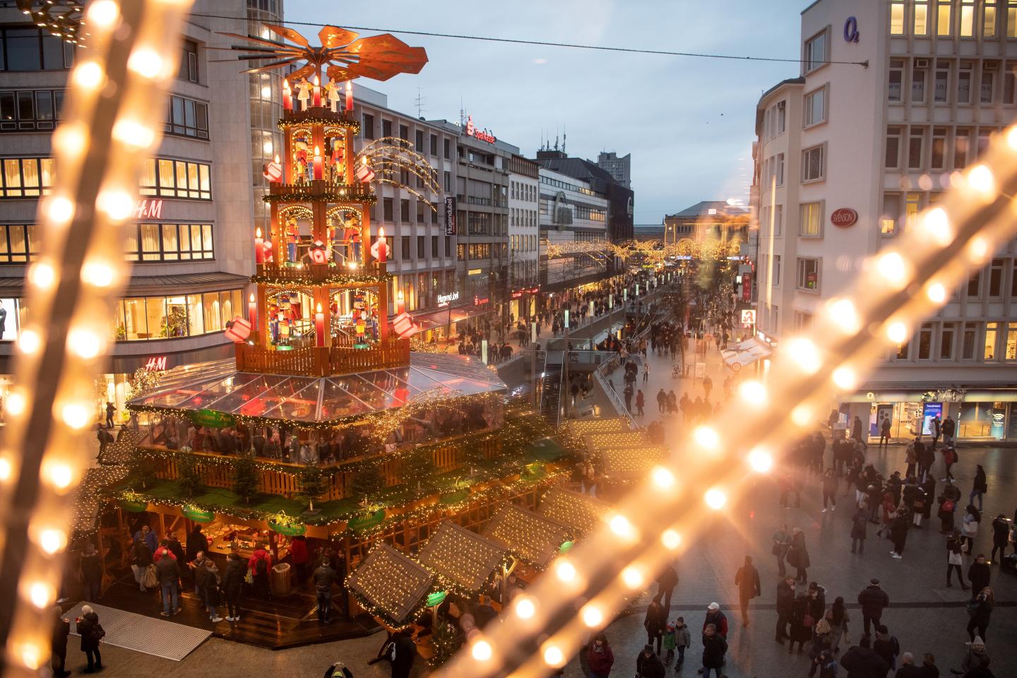 In the immediate foreground, two strands of string lights. In the background, a Christmas-themed carousel in the middle of an open-air mall.