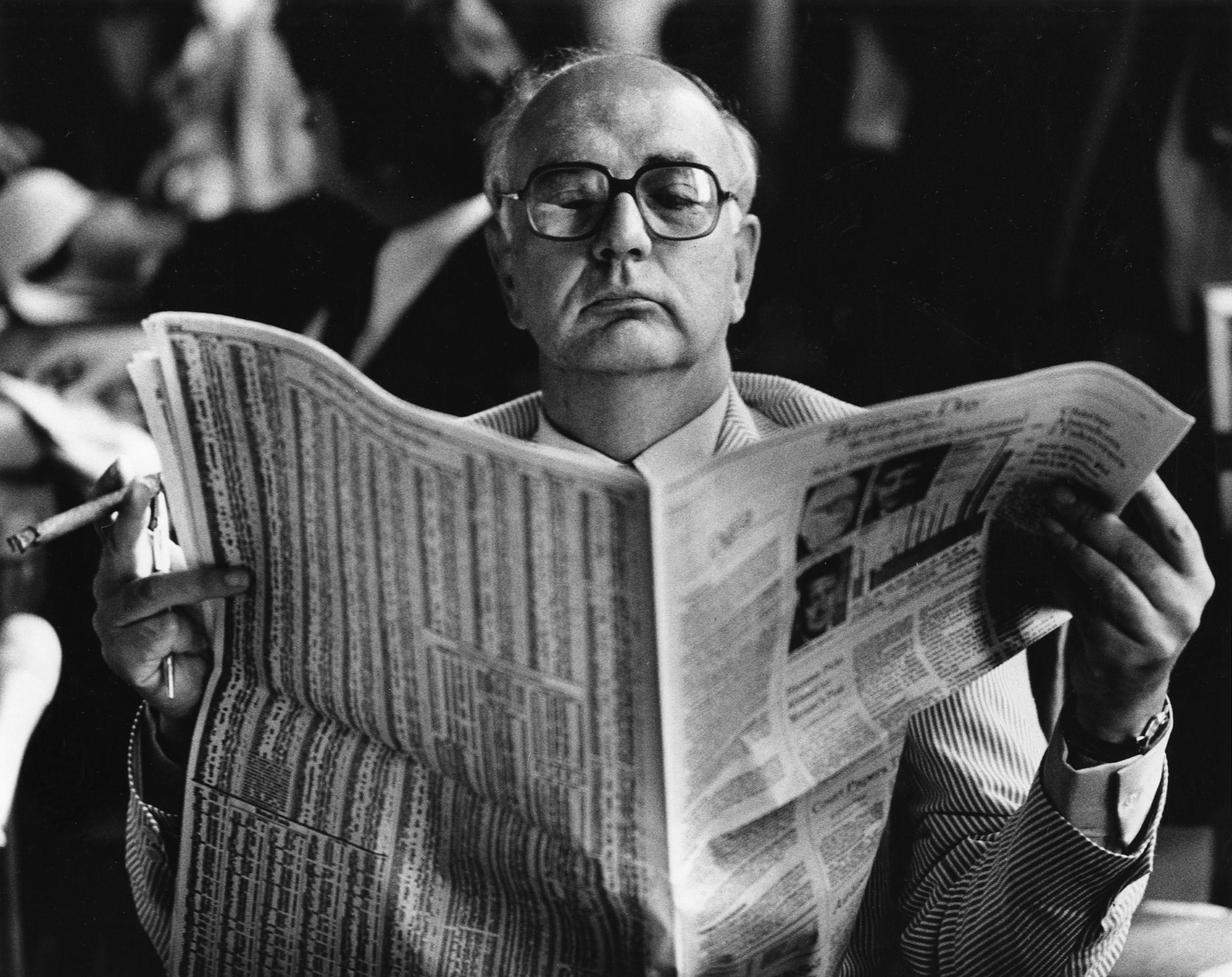 FRB Chairman Paul Volcker reading the financial page as he waits for a hearing
