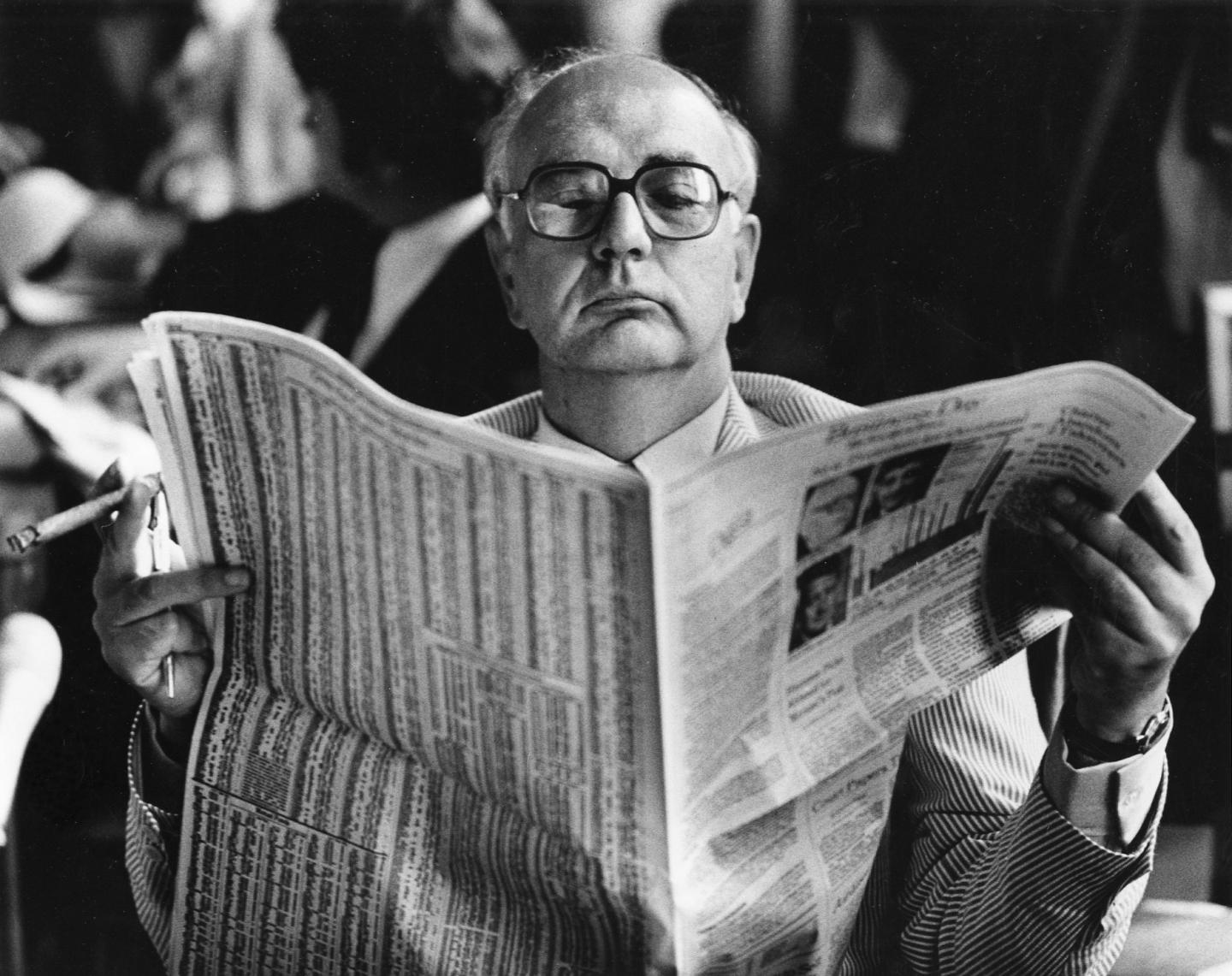 FRB Chairman Paul Volcker reading the financial page as he waits for a hearing