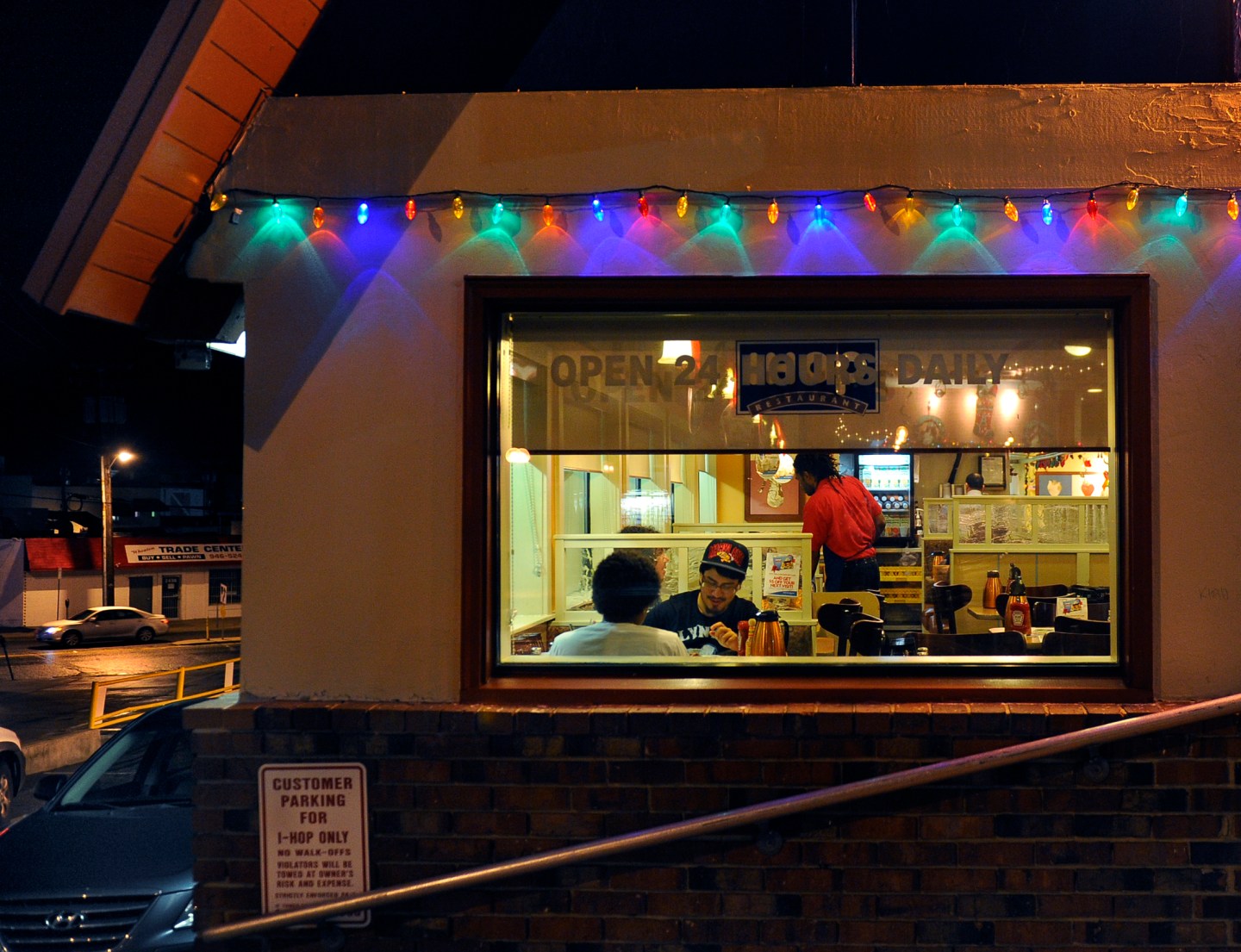 An IHOP is decorated with one string of Christmas lights. You can see through the window to see people eating.