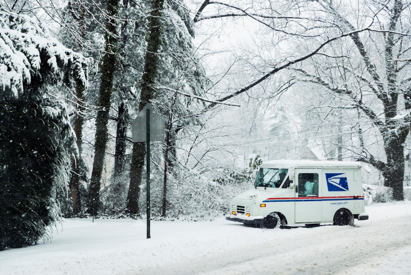 A USPS mail truck is pulled off to the side of the road in a snow storm.