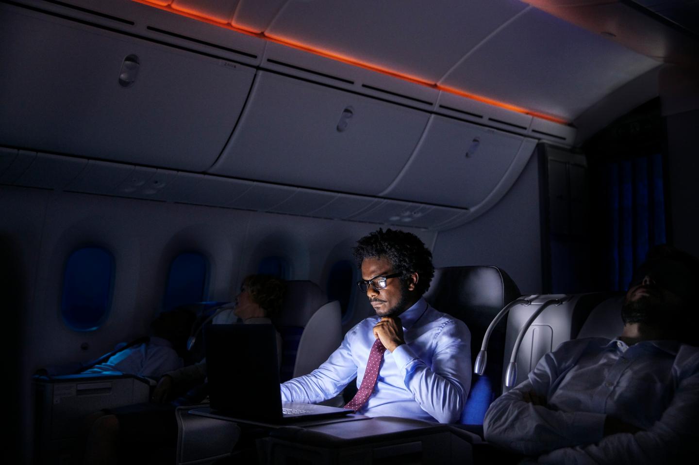 Businessman working at laptop on night airplane