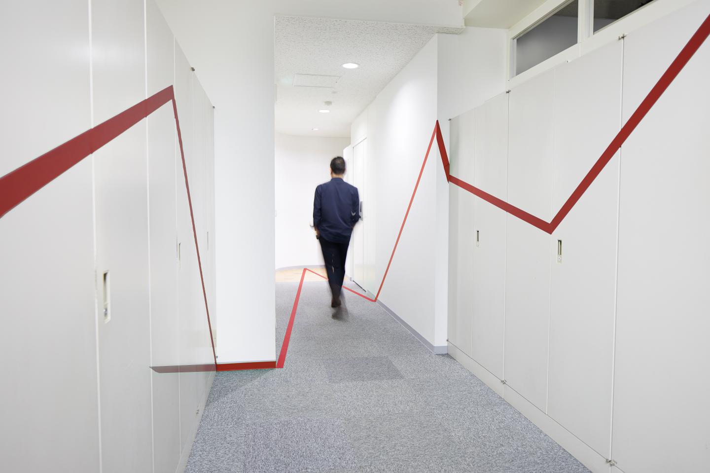 a red graphic chart on the wall and floor of the corridor, and a man walking