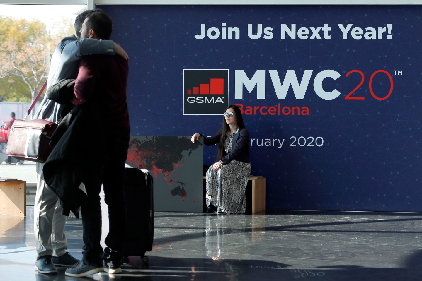 A woman looks at two visitors hugging each other on the last day of the Mobile World Congress (MWC) in Barcelona on February 28, 2019.
