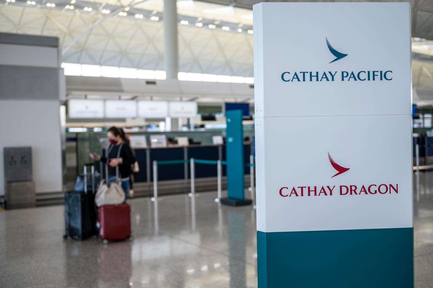 A passenger checks her phone as she stands next to a stand with Cathay Pacific and Cathay Dragon on it inside the terminal of the Hong Kong International Airport on February 22, 2020 in Hong Kong, China. the coronavirus or Covid-19 which originated from Wuhan China has infected over 77,000 and killed 2361 worldwide to date, passenger flights into and out of the Hong Kong has drop by two-thirds with airlines cancelling flights and travellers plummet because of the Coronavirus in Hong Kong. (Photo by Vernon Yuen/NurPhoto via Getty Images)